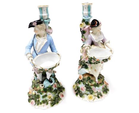 A pair of late 19thC Sitzendorf porcelain figural candlesticks, modelled as a gallant and lady, holding a floral encrusted ba