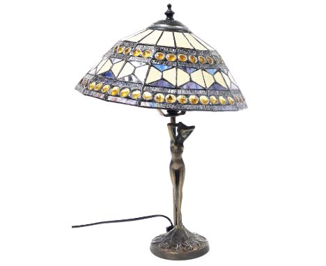 A Tiffany style table lamp, with a geometric panelled and jewel shade, raised on a stem fronted by a nude figure of a lady, a