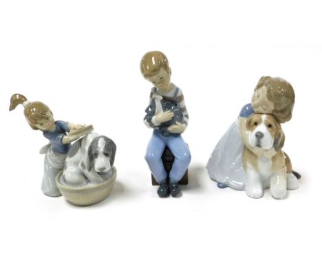A Lladro Porcelain figure of a girl kneeling washing her dog in a tub, and two Nao figures, one of a boy seated with a puppy,