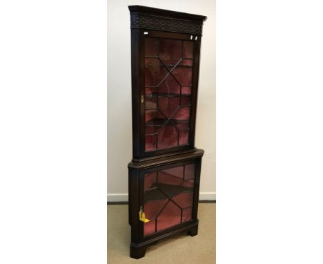 A modern reproduction mahogany corner cabinet with blind fretwork carved frieze over two astragal glazed doors, raised on bra