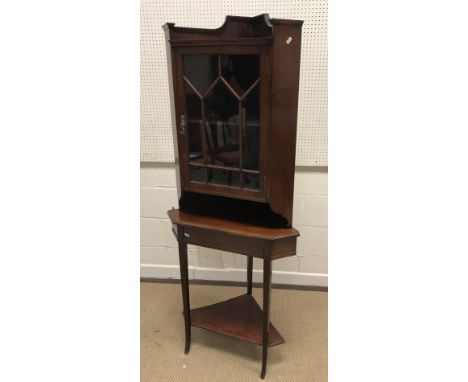 An Edwardian mahogany corner cupboard with glazed door enclosing a single shelf, raised on a plain stand of square tapered le