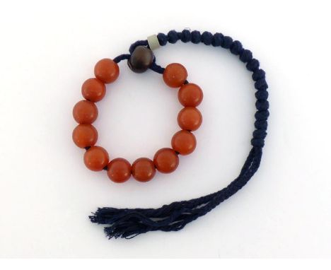 A string of twelves Chinese carved red agate beads and one brown agate bead with jade stopper and tassel. Agate in even red t