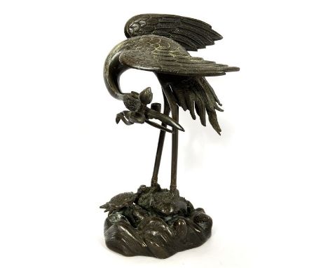 A Japanese bronze figure of a crane, Meiji Period style, modelled with head bowed and holding a water lily, a terrapin at its