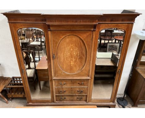 An Edwardian mahogany triple wardrobe, with a moulded cornice above a central cupboard and drawers flanked by mirrored doors 