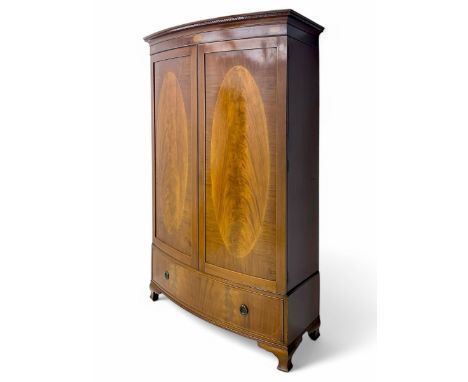 Early 20th century mahogany bowfront double wardrobe, dentil-moulded cornice over twin doors with large oval flame-inlaid pan