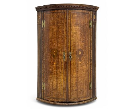 George III oak bowfront corner cupboard, the dentil-moulded cornice above twin doors inlaid with stylised urn motifs and cant