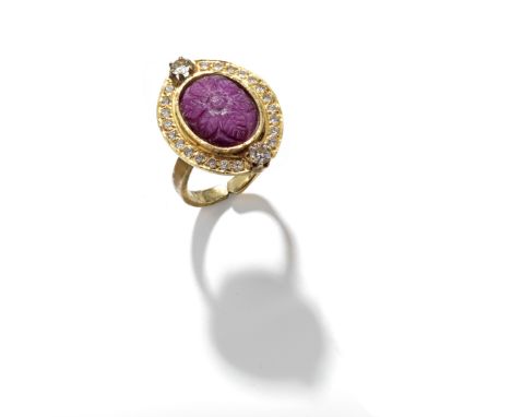 A carved ruby and diamond set ring, the oval-shape ruby has carved foliate decoration and is set in a surround of round brill