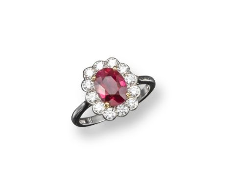 A ruby and diamond cluster ring, the oval-shaped ruby is set with twelve round brilliant-cut diamonds in 18ct white gold. Lon