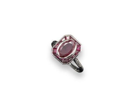 A ruby cluster ring, the oval-shaped ruby is set within a surround of tapered baguette-shaped rubies in platinum with two sma