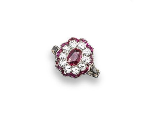 An Edwardian ruby and diamond cluster ring, the oval shaped ruby is millegrain-set within a surround of old circular cut diam