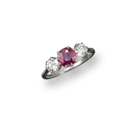 A ruby and diamond three stone ring, the cushion-shaped ruby is set between two old circular-cut diamonds in platinum. Size M