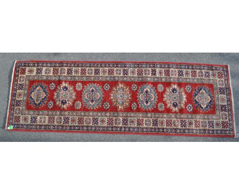 A 20th century super Kazak runner carpet floor rug. Having a red ground, with geometric and foliate design central medallions