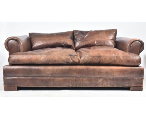 A modern high-end British Design two seater leather sofa. The sofa having scrolled elbow rests raised on bun feet. In brown t