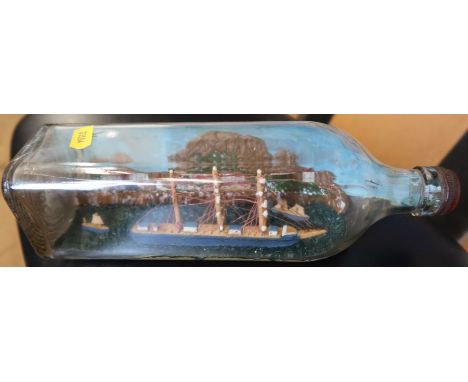 A model ship, in a square shaped bottle, with painted back drop