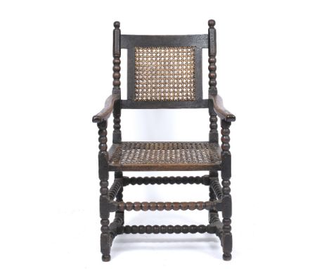 A CHARLES II OR WILLIAM AND MARY PERIOD OAK CARVED ARMCHAIR with bobbin turned supports to the caned back, shaped arms, caned