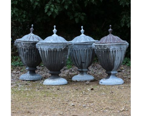 A SET OF FOUR ADAMS STYLE LEAD URNS AND COVERS each with a turned finial, with fluted bodies decorated with female masks stoo