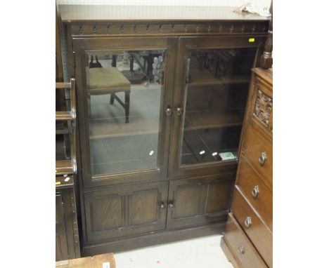 An Ercol dark oak dresser, the glazed cupboard above a base of two panelled doors, an Ercol dark oak glazed bookcase cabinet,