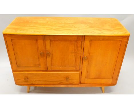 An Ercol light elm sideboard, with a shaped top above a single door, flanked by a pair of panelled doors above a drawer, on t