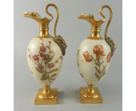 A pair of Royal Worcester blush ivory ground porcelain ewers, each painted with flowers picked out in gilt, the handles termi