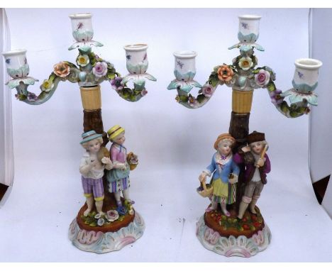 A pair of late 19th Century Continental ceramic candlesticks, with two figures and floral decoration, marks to the base, each