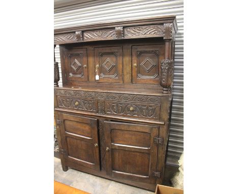 An 18th Century and later oak carved court cupboard, the canopy with green forest cornice over three panel doors with turned 
