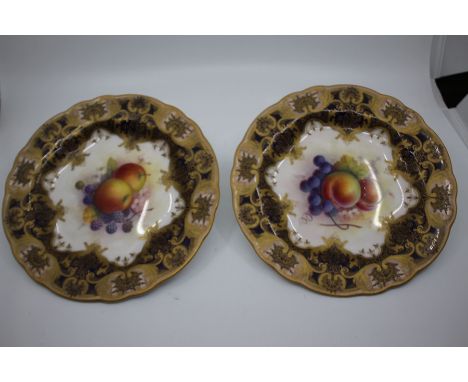 A pair of Royal Worcester cabinet plates painted by A Shuck, central still lifes with fruit, the cobalt borders with gilt lam