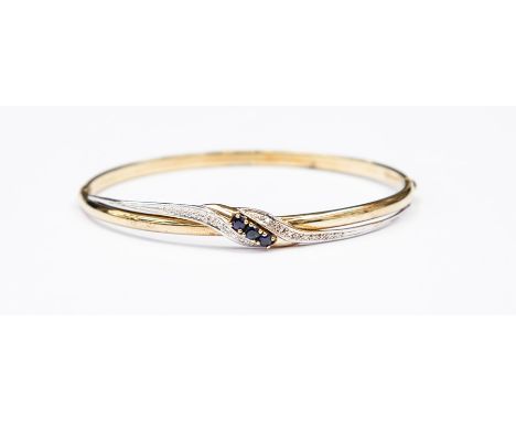 A sapphire and diamond 9ct gold bangle, comprising three round cut sapphires set to the front with&nbsp; a cross over design 