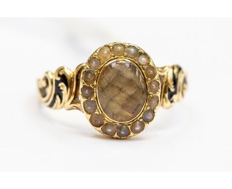 A Victorian mourning ring, the oval glazed hair compartment with a seed pearl surround, scrolled foliate shoulders decorated 