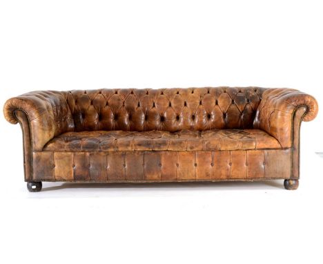 A Chesterfield Sofa, upholstered in worn brown buttoned leather, with rounded back support, arms and overstuffed seat above c