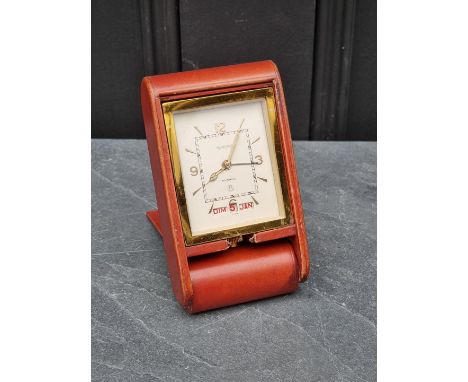 A vintage red leather and brass folding travel alarm clock, by Jaeger-LeCoultre for Dunhill, 12cm wide when folded. 