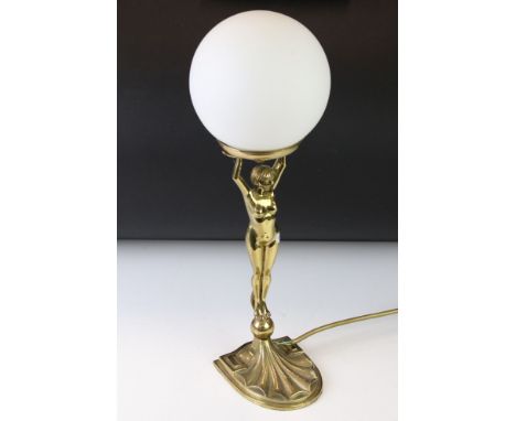 Art deco style brass table lamp modelled as a nude lady holding a globe aloft, with opaque white glass lamp shade. Measures a