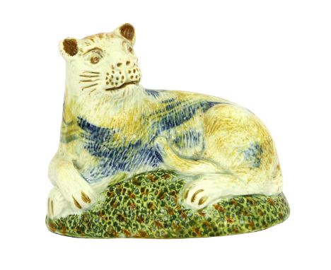 A Prattware Lioness, circa 1800, modelled recumbent, with ochre markings on a green, blue and ochre mound base 9cm longProven