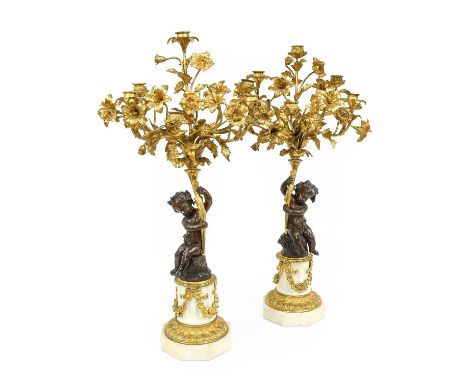 A Pair of French Gilt and Patinated Bronze Six-Light Candelabra, in Louis XVI style, with foliate sockets and drip pans on le