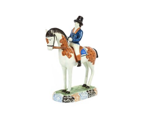 A Prattware Equestrian Group, circa 1800, as a gentleman wearing a black hat and blue coat mounted on a skewbald horse, on a 
