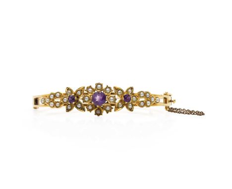 A 9ct gold amethyst and seed pearl floral bangle,  with three graduated flowerheads with a central round cut amethyst and spl