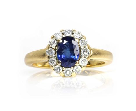 An 18ct gold sapphire and diamond cluster ring,  with an oval cut sapphire, four claw set to a surround of round brilliant cu