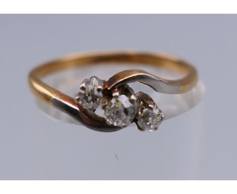 An 18 ct gold and platinum three stone diamond crossover ring. Ring size N. 2.3 grammes total weight.