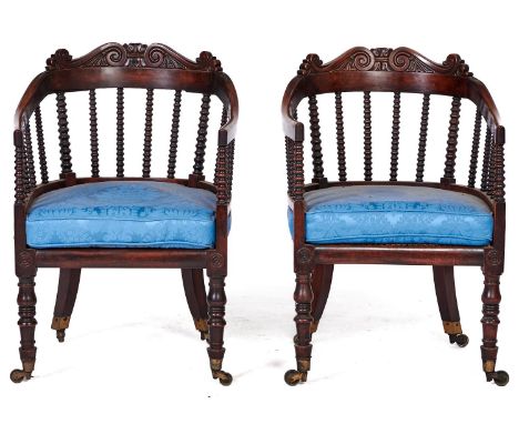 A pair of Victorian mahogany bergeres, c1850, the back hoop on bobbin turned spindles and crested by carved scrolls, on balus