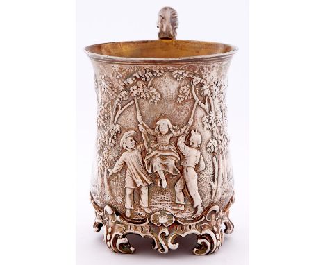 A Victorian silver christening mug, of baluster form, embossed with three children playing on a swing between trees, leafy sc