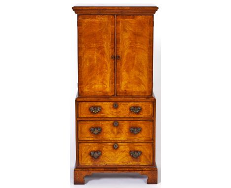 A walnut cabinet, 1980's, in George II style, enclosed by a pair of feather banded doors above drawer and fall-front as three