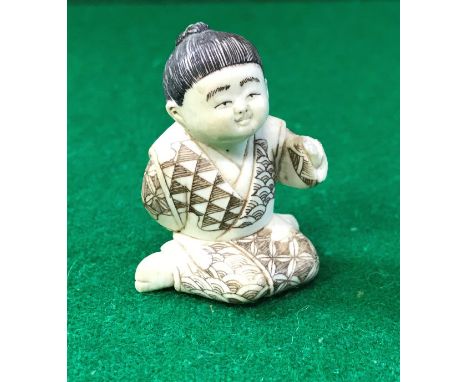 An early 20th Century Chinese carved ivory netsuke as a young kneeling boy bearing script, signature to base