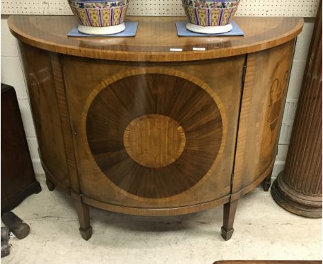 A 19th Century walnut and inlaid demi-lune cabinet in the Sheraton style, the plain top above a cupboard door opening to reve