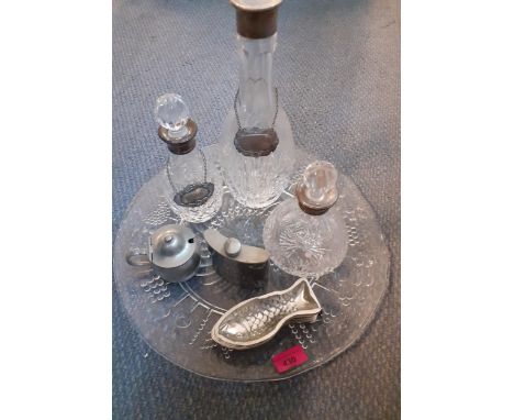 A large glass platter together with three decanters with white metal collars and two decanter labels, one silver and other it