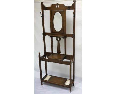 ARTS AND CRAFTS OAK HALL STAND
with a shaped top rail above an oval bevelled mirror with shelf below, surrounded by six coat 