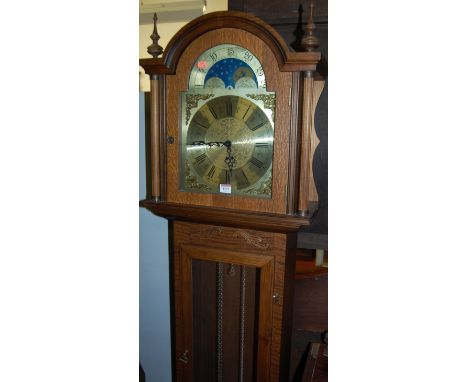 A contemporary oak longcase clock having a glazed trunk door, arch moon phase dial and three train movement