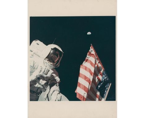 Eugene CernanHarrison Schmitt with the Earth above the deployed American flag, the photographer reflected in the visor; EVA 1