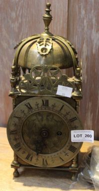 A reproduction brass Lantern clock, fitted bell strike to top, silvered chapter ring with Roman numerals surrounding a floral