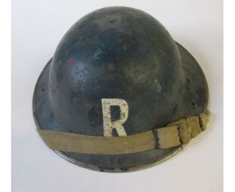 A WW2 metal helmet, painted blue with "R" in white to one end, indistinctly impressed to the rim