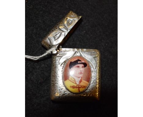 A silver coloured metal rounded rectangular vesta case, applied with an oval enamel panel printed with a jockey 