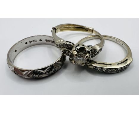 Three white metal rings. Comprising an 18ct gold wedding ring, with diamond cut pattern; a white metal diamond solitaire ring